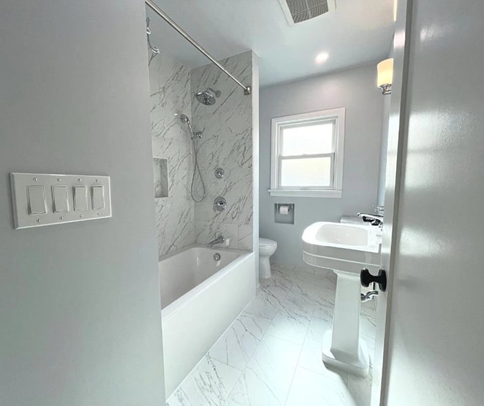 An outdated 1920's bathroom remodeled with clean white tile and chrome fixtures. 