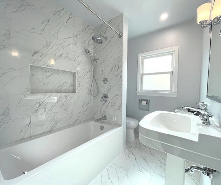 An angled view of the bathroom remodel which features marble like tile, a deep soaking tub, and chrome fixtures.